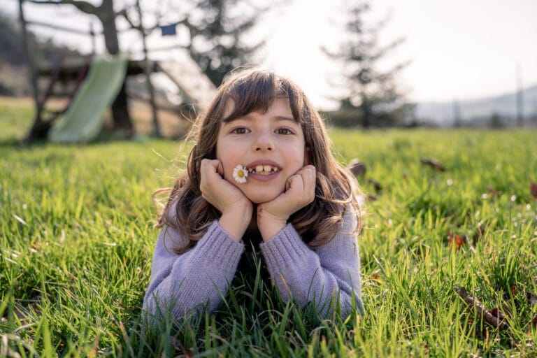 Une petite fille couchée dans l'herbe avec une marguerite dans la bouche. Prise a Peyrins