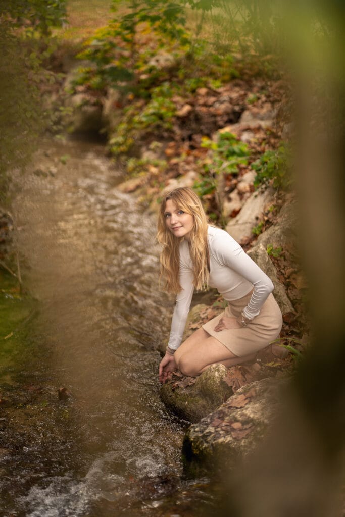 Une jeune femme assise a genoux au bord d'une rivière en forêt, dans le boix des Naix a Romans-Sur-Isère.