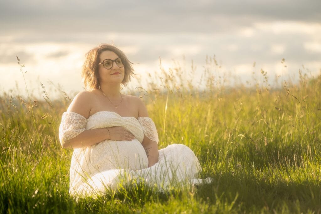 Femme enceinte assise dans l'herbe pendant un couché de soleil, regardant vers l'avenir