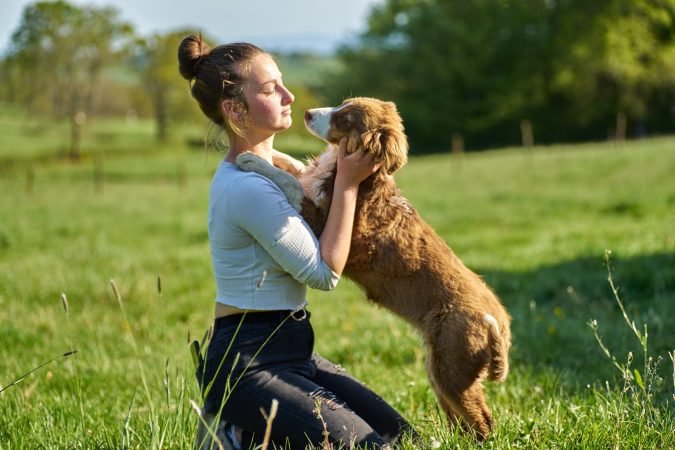 Jeune femme faisant un câlin a son berger australien marron, dans un champ bien vert