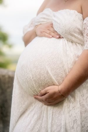 Gros plan du ventre rond d'une femme en pleine grossesse (enceinte) portant une robe blanche